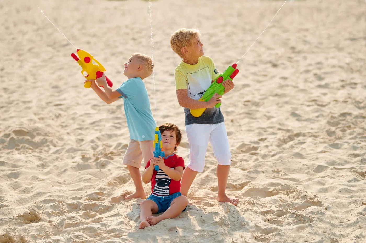 Enfants qui rient en jouant avec des pistolets à eau dehors au soleil lors d'une fête